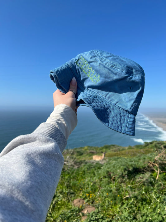 Formula S7 Sustainable Bucket Hat held against an ocean cliff view scenery with a deer
